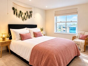 A bedroom with a large bed, a bedside table with a lamp, a window with a view, and a macrame wall hanging. - Stylish apartment on the Poole Quay-free parking 2 mins away (Poole)
