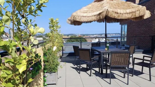 Une terrasse extérieure avec une table et des chaises, un parasol en chaume et une vue sur le paysage urbain.
