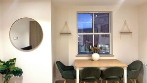 Un coin repas comprenant un miroir rond, une table en bois et trois chaises vertes.