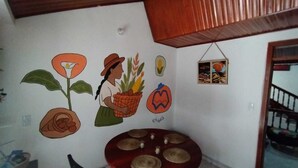 Habitación con pared blanca decorada con murales de temática agrícola, techo de madera y una pequeña mesa con superficie roja.