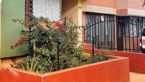 Un hotel con fachada verde y beige, una señal visible y un balcón con plantas.