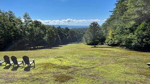 A grassy field with three Adirondack chairs facing a forested area. - True Adirondack Retreat! Nestled in the Mountains! (Mayfield)
