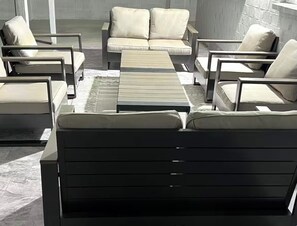 Ein moderner Außenbereich zum Sitzen mit einer Couch, Stühlen, einem Couchtisch und einem gemusterten Teppich.