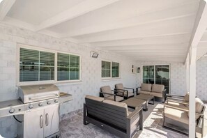 Eine Terrassenanlage im Freien mit Grill, Sitzgelegenheit und einer Glastür zu einem überdachten Bereich.
