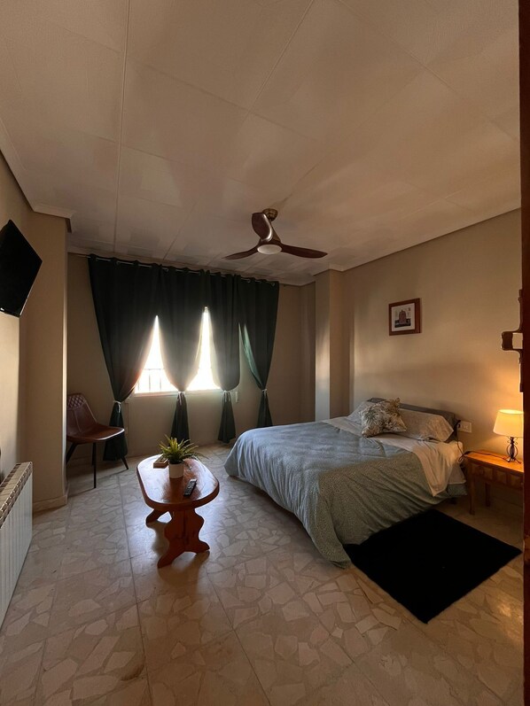 A bedroom with a bed, a desk, a chair, a ceiling fan, and a window with curtains. - El Refugio Bed & Breakfast (Villarrobledo)