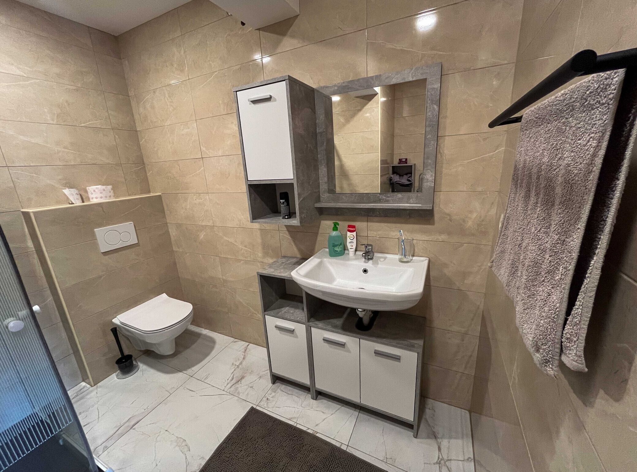 A modern bathroom with a toilet, sink, mirror, and towel rack.