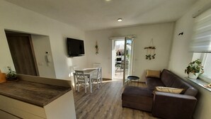 Ein modernes Wohnzimmer mit einem braunen Sofa, einem Esstisch mit Stühlen, einem an der Wand befestigten Fernseher und Holzböden.