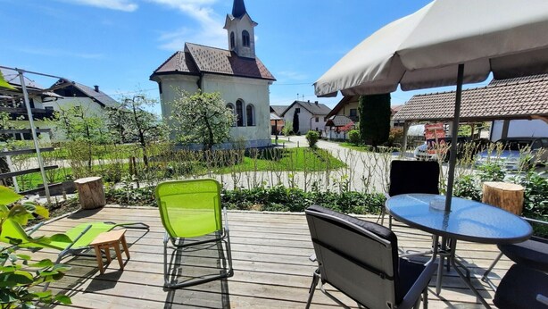 Eine Holzterrasse mit Sitzgelegenheit, im Hintergrund eine Kirche und ein klarer Himmel.