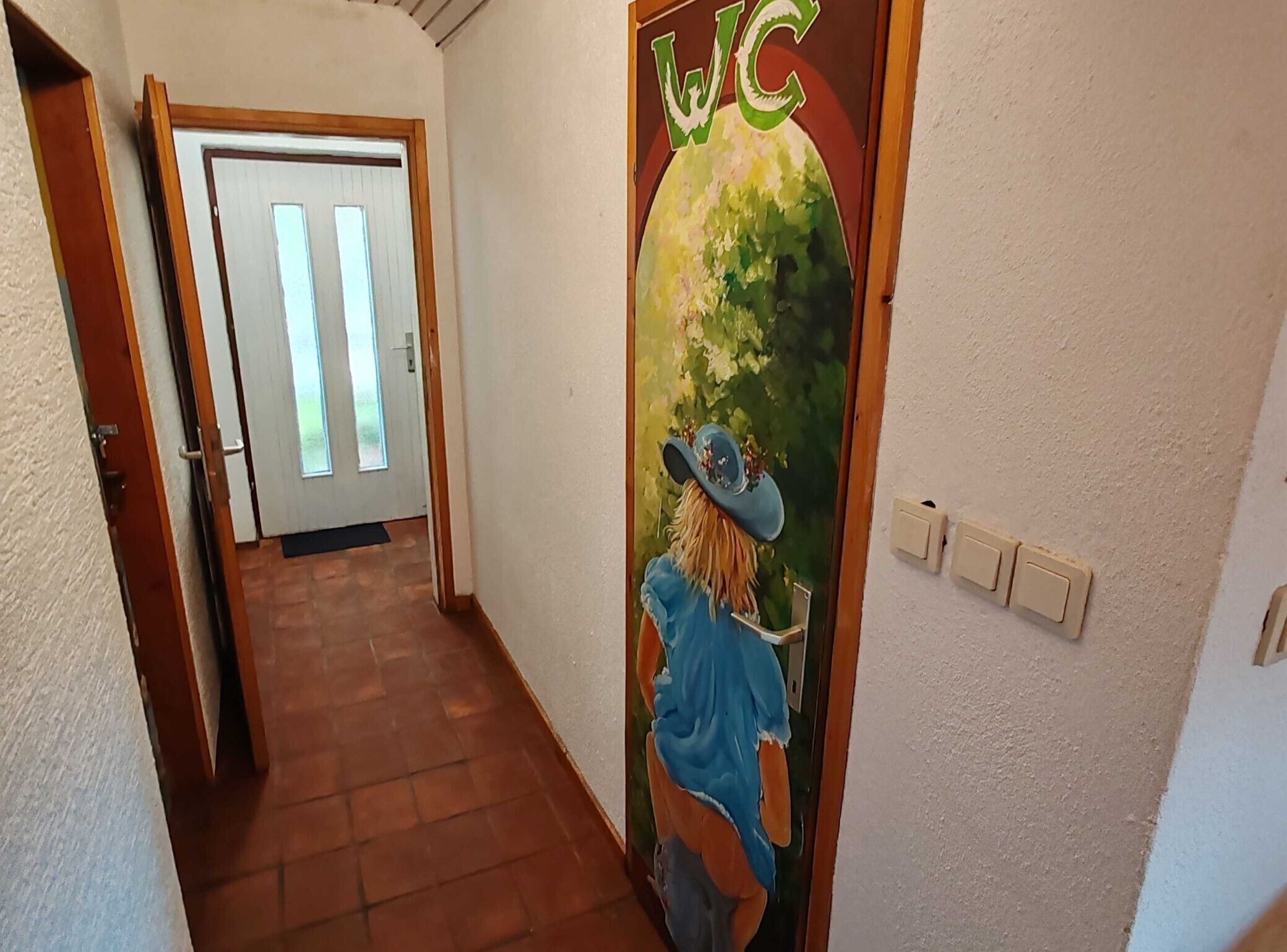 A hallway with a door at the end, a wall-mounted light switch, and a door with a decorative sticker.