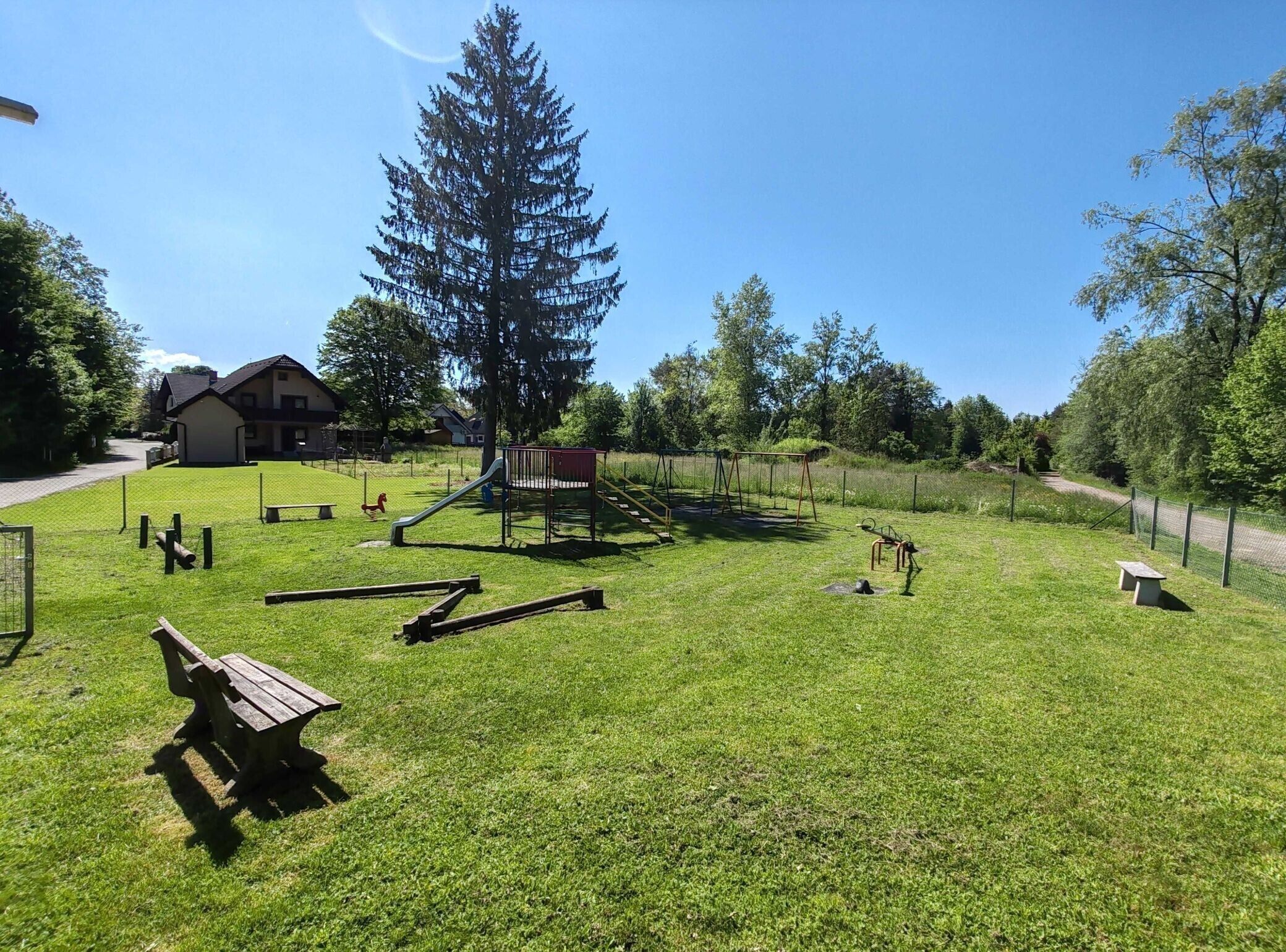 A playground with a slide, swings, and a climbing structure, surrounded by a grassy area and trees.