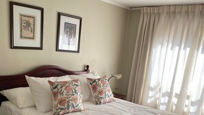 A neatly made bed with floral pillows, a beige blanket, and a rolled towel. There are two framed pictures on the wall above the bed.