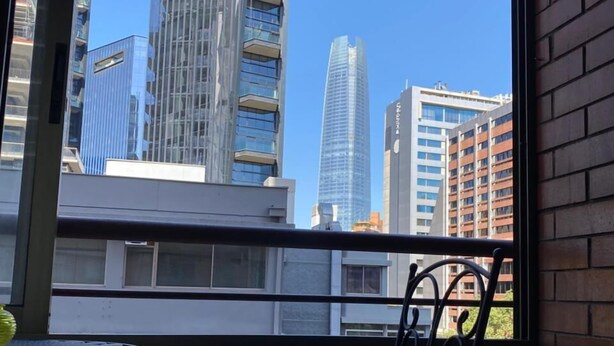 A balcony with a view of modern buildings, a metal chair, and a small table.