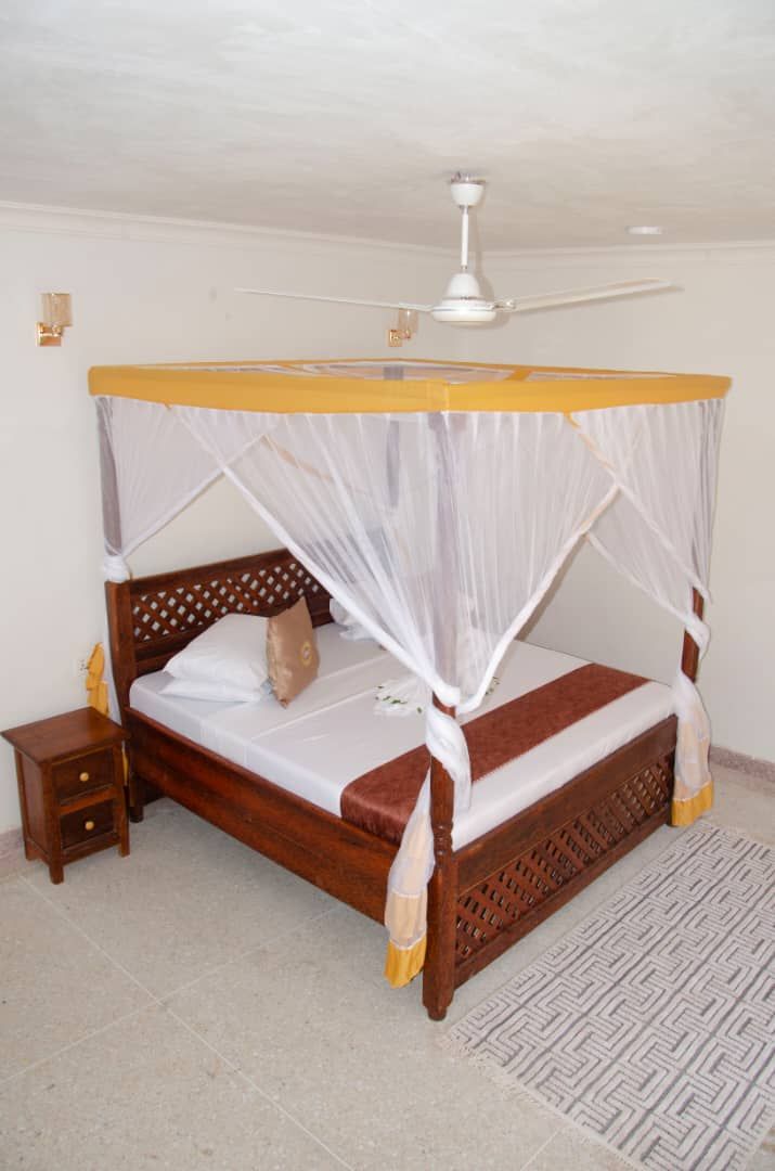 Una cama individual con estructura de madera y dosel, una mesita de noche y un ventilador de techo.