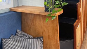 Rincón de una habitación con un banco de madera, una planta en maceta y una escalera negra.