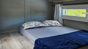 Un dormitorio compacto con una cama individual, una ventana con cortinas y vistas a zonas verdes.