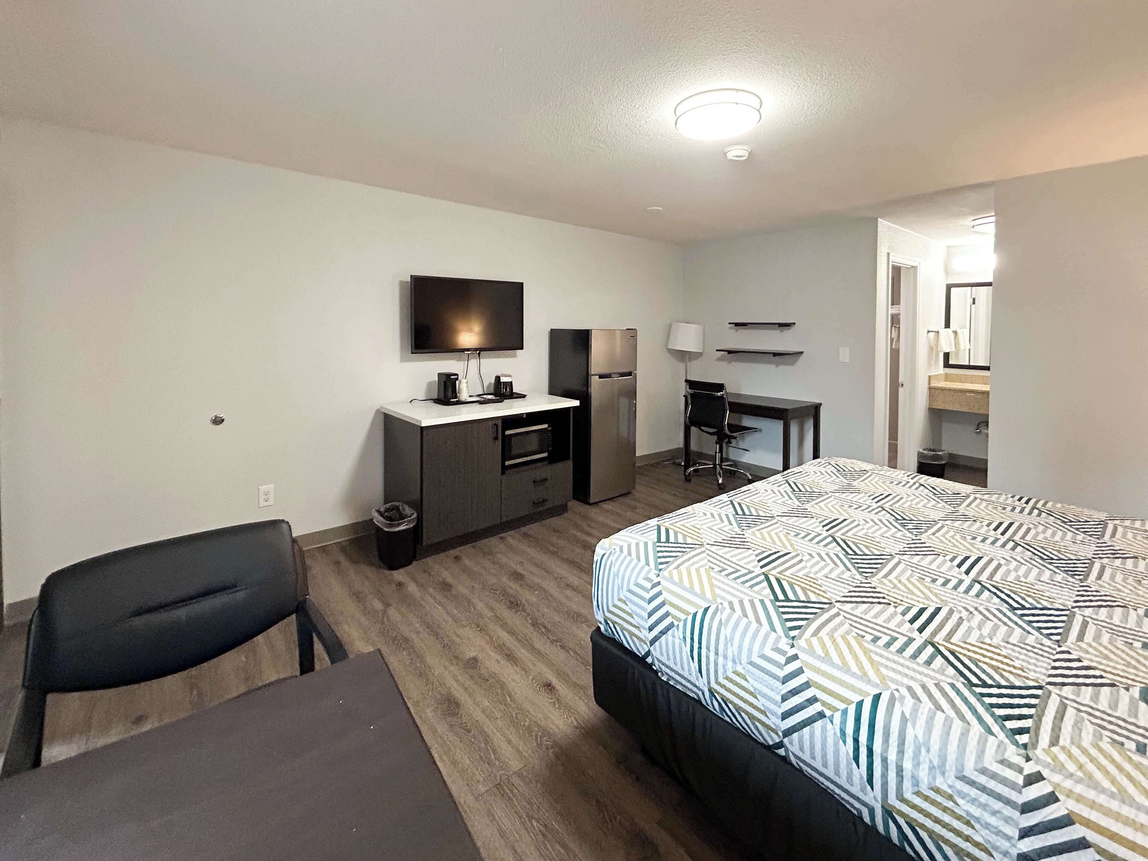Hotellihuone, jossa on sänky, työpöytä, tuoli, televisio, jääkaappi ja roskakori.