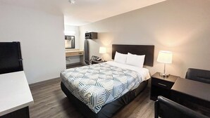 A hotel room with a bed, bedside table, chair, desk, and a small kitchenette area. - Studio 6 Suites Vancouver, Wa - Waterfront (Vancouver)