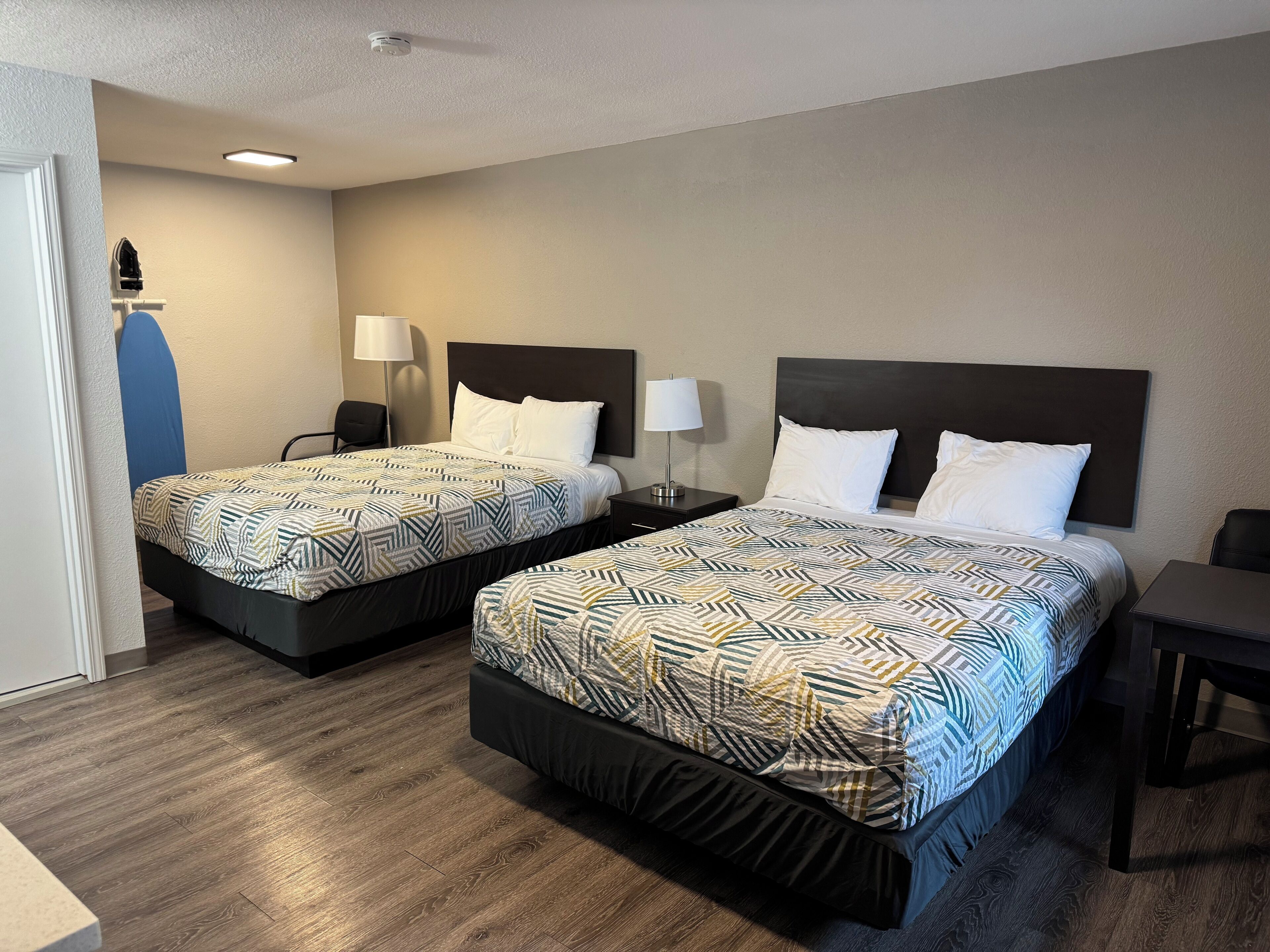 Habitación de hotel con dos camas, cada una con una colcha estampada, lámparas de noche y un escritorio.