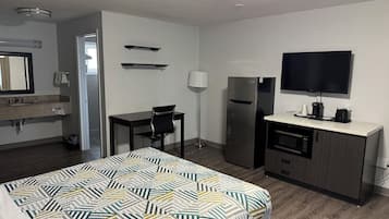 Habitación de hotel con cama, escritorio, refrigerador, televisión y microondas.