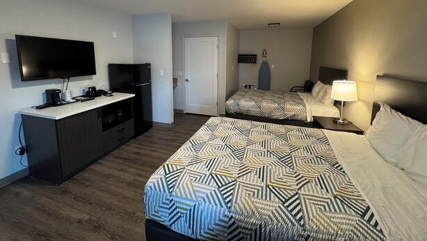 A hotel room with two beds, a TV, a desk, and a kitchenette.