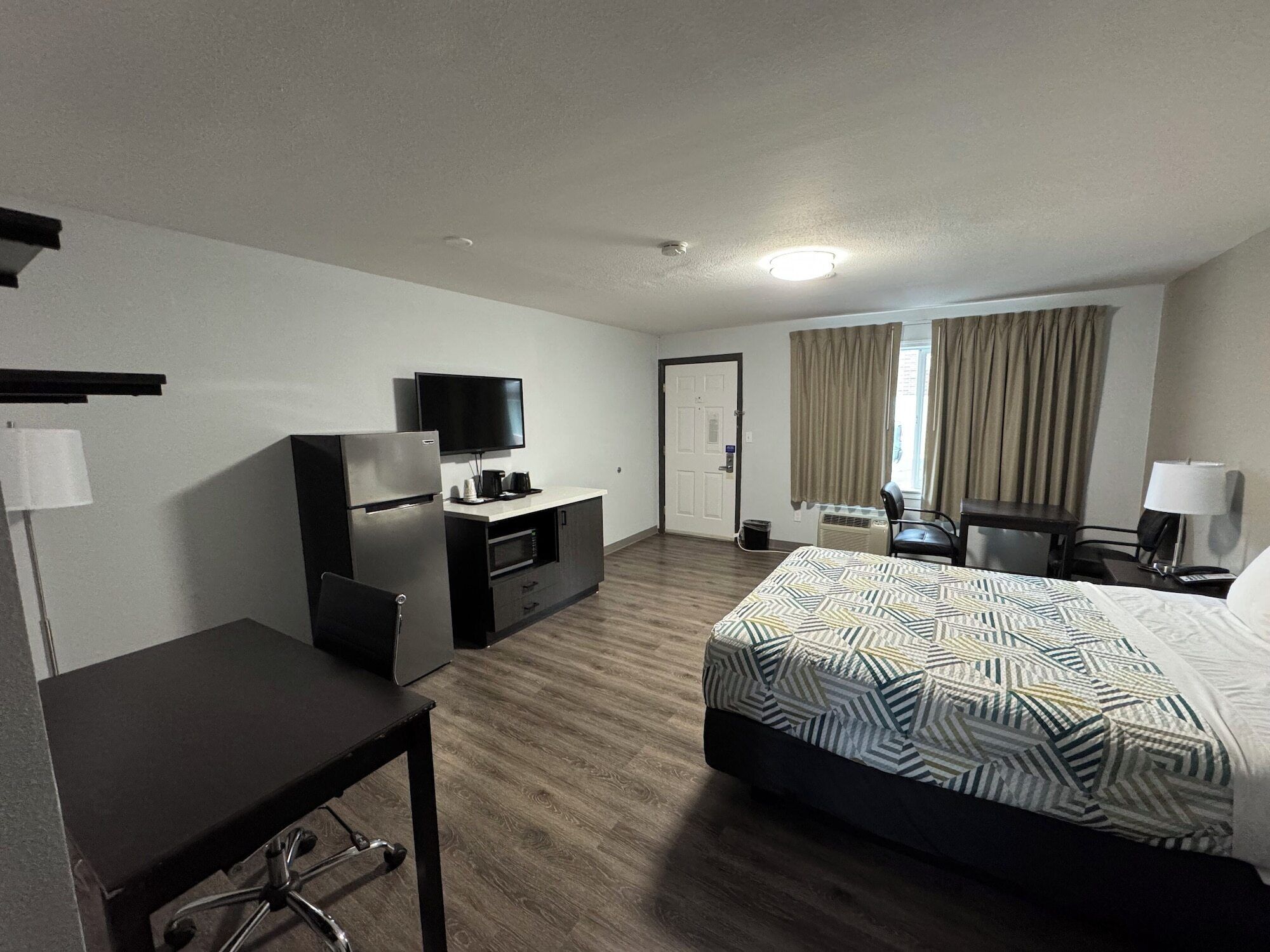 A hotel room with a bed, a desk, a refrigerator, a television, and a door.