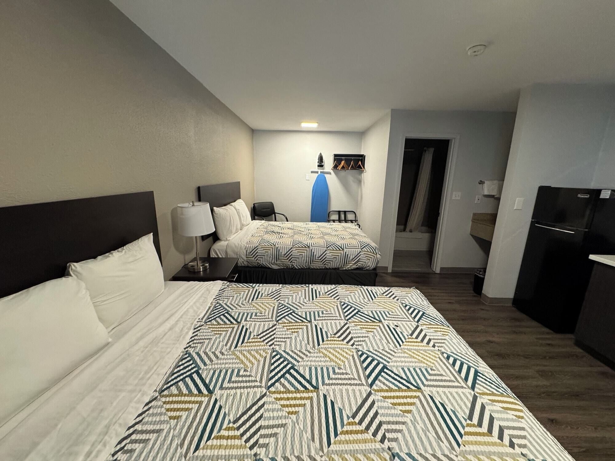 A hotel room with a large bed, a desk, a chair, a wardrobe, and a bathroom visible through an open door.