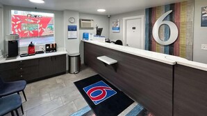 A reception area with a counter, chairs, a trash bin, and a wall-mounted clock. - Studio 6 Suites Vancouver, Wa - Waterfront (Vancouver)