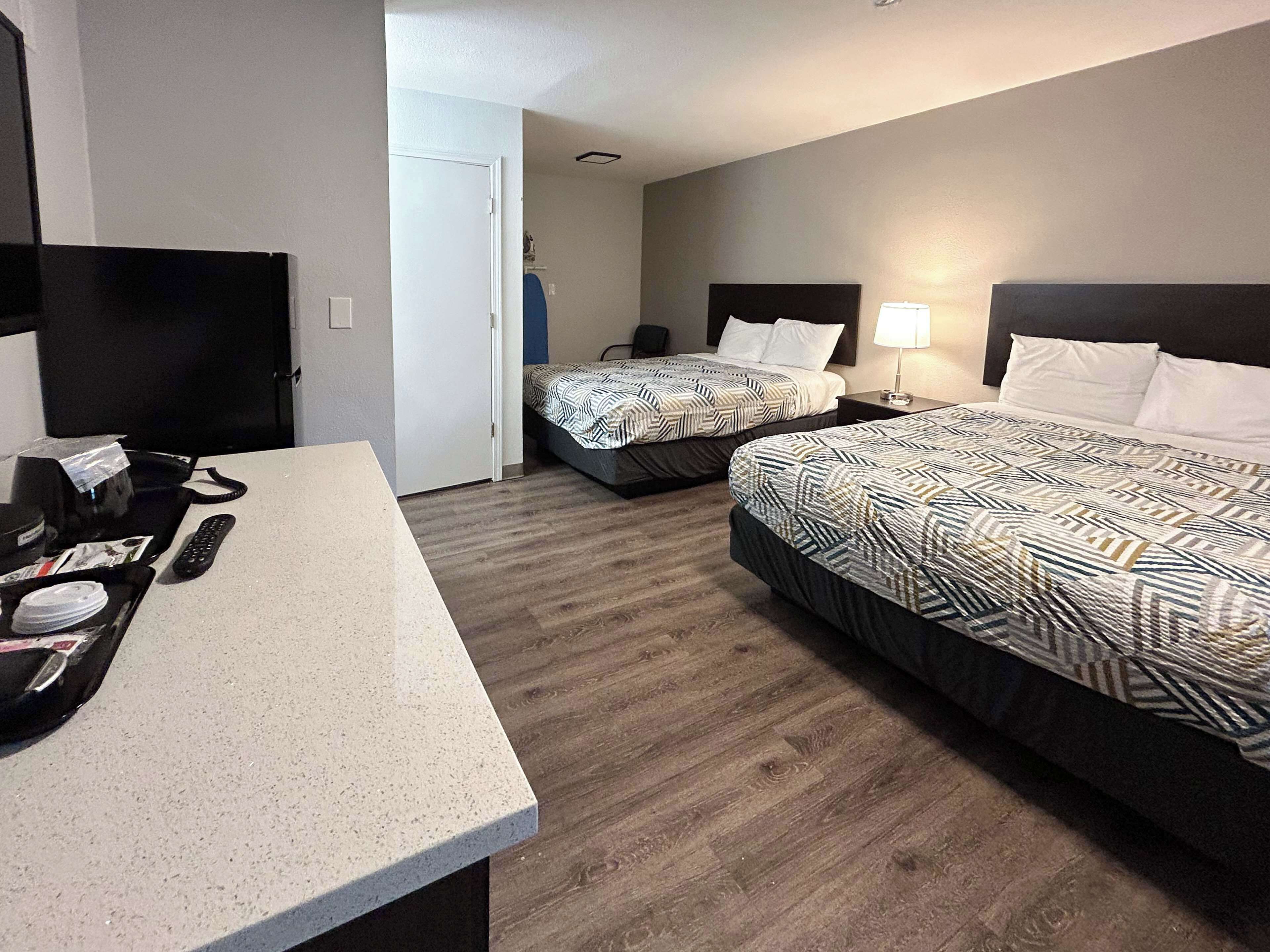 Quarto de hotel com duas camas, uma escrivaninha com telefone e controle remoto, e uma televisão.