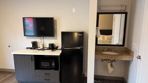 A hotel room with a kitchenette, a flat-screen TV, a refrigerator, a microwave, a coffee maker, and a sink with a mirror above it. - Studio 6 Suites Vancouver, Wa - Waterfront (Vancouver)