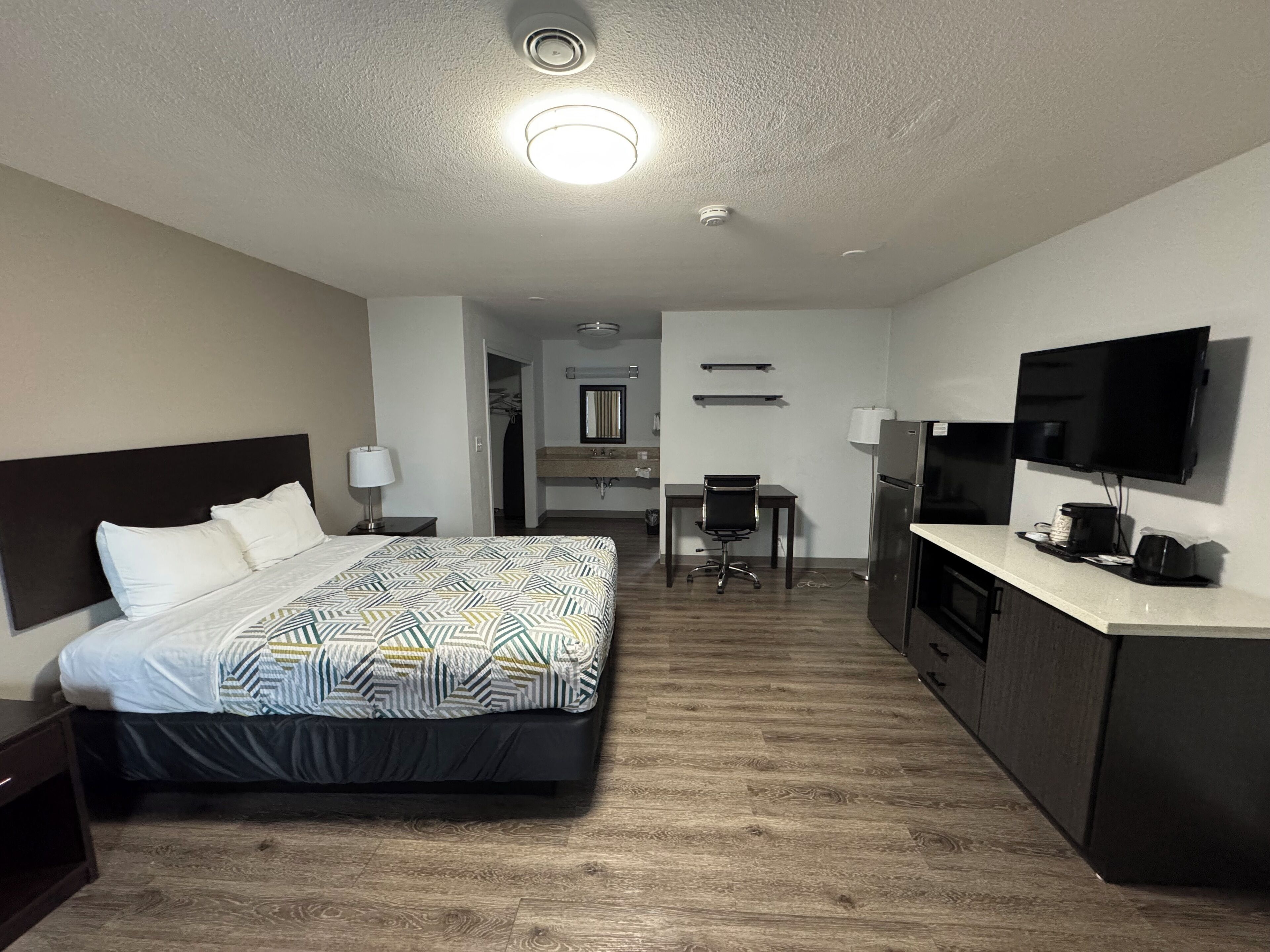 Ein Hotelzimmer mit Bett, Schreibtisch, Stuhl, Fernseher und einer Küchenzeile.