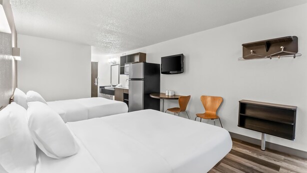 A modern hotel room with two beds, a small kitchenette, a TV, and a seating area with chairs. - Studio 6 King Of Prussia, Pa - Philadelphia (Wayne)