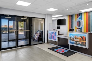 A hotel reception area with a glass door entrance, a reception desk, and a colorful wall with a large number '6'. - Studio 6 King Of Prussia, Pa - Philadelphia (Wayne)