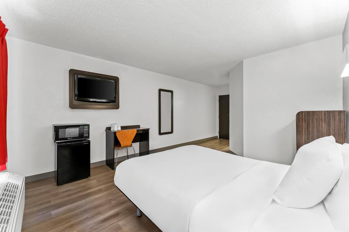 Ein Hotelzimmer mit Bett, Schreibtisch, Stuhl, Fernseher und einer Mikrowelle.