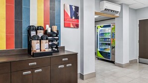 A hotel reception area with a coffee station, a vending machine, and a poster on the wall. - Studio 6 King Of Prussia, Pa - Philadelphia (Wayne)