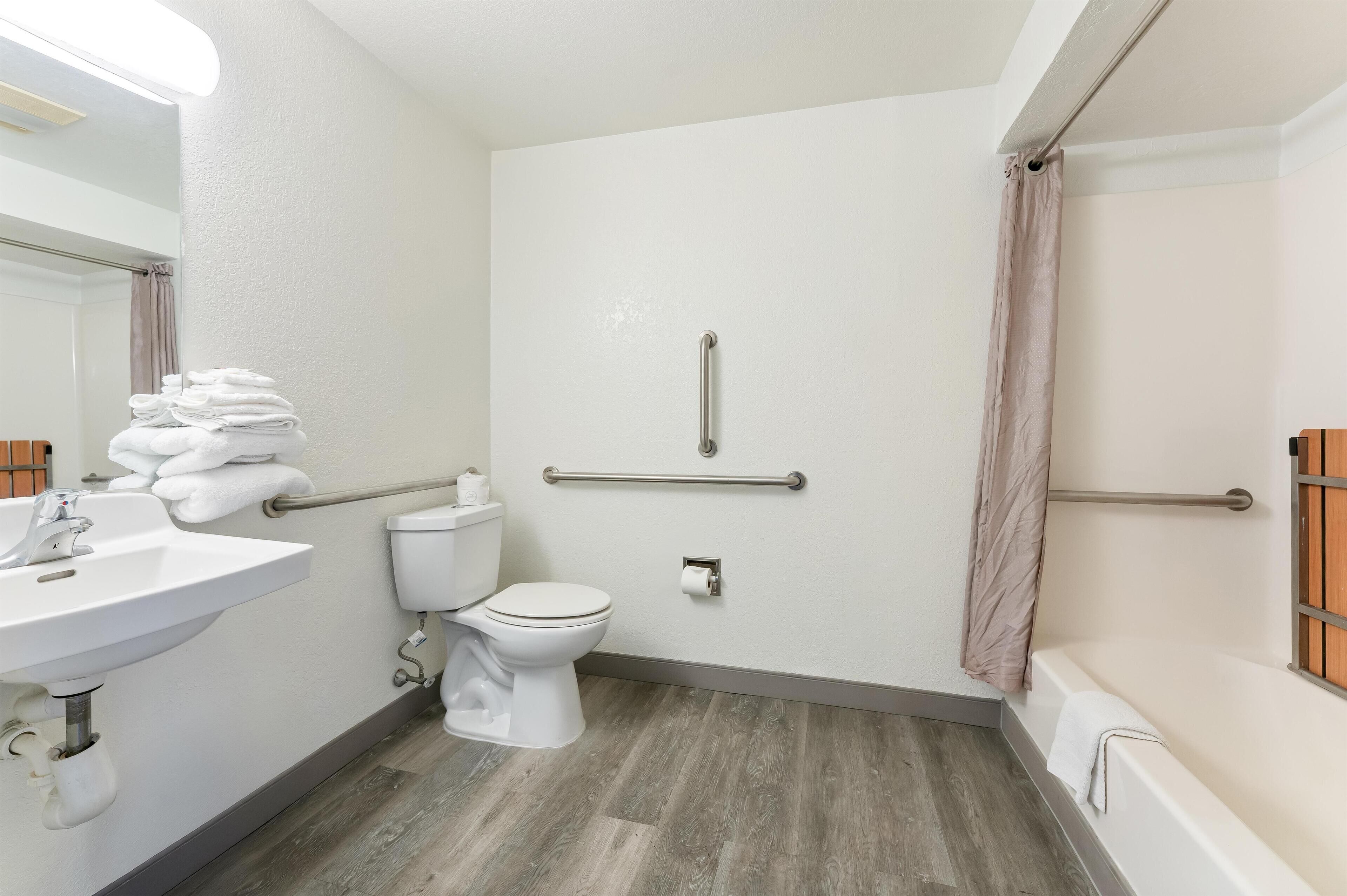 A bathroom with a white sink, toilet, and bathtub. There are handrails on the walls and a towel rack with towels.