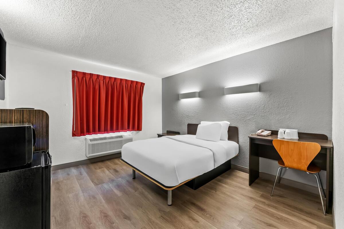 Ein modernes Hotelzimmer mit Bett, Schreibtisch, Stuhl und Fernseher.