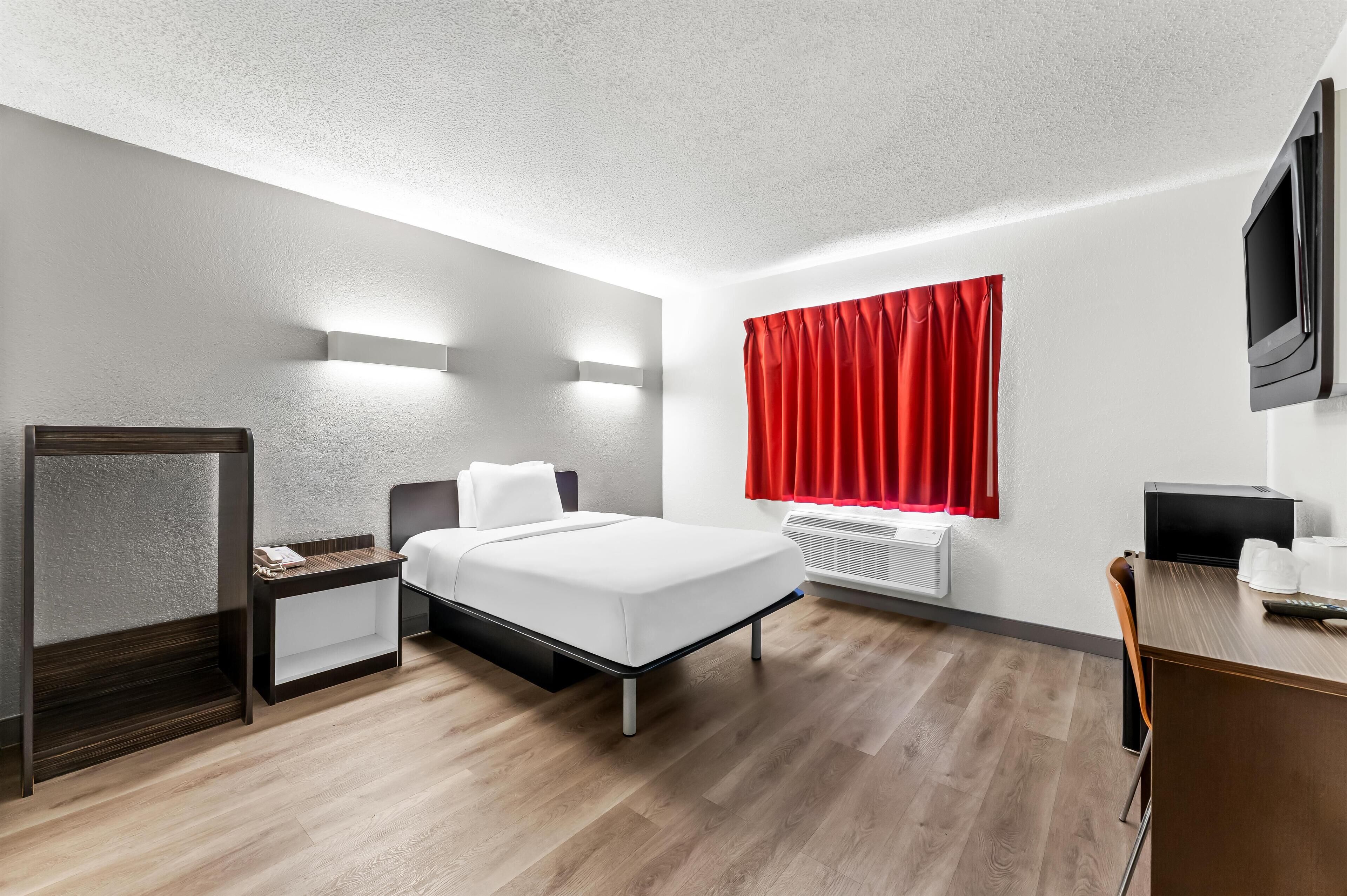 Habitació d'hotel moderna amb llit, taula de nit, escriptori i televisió.