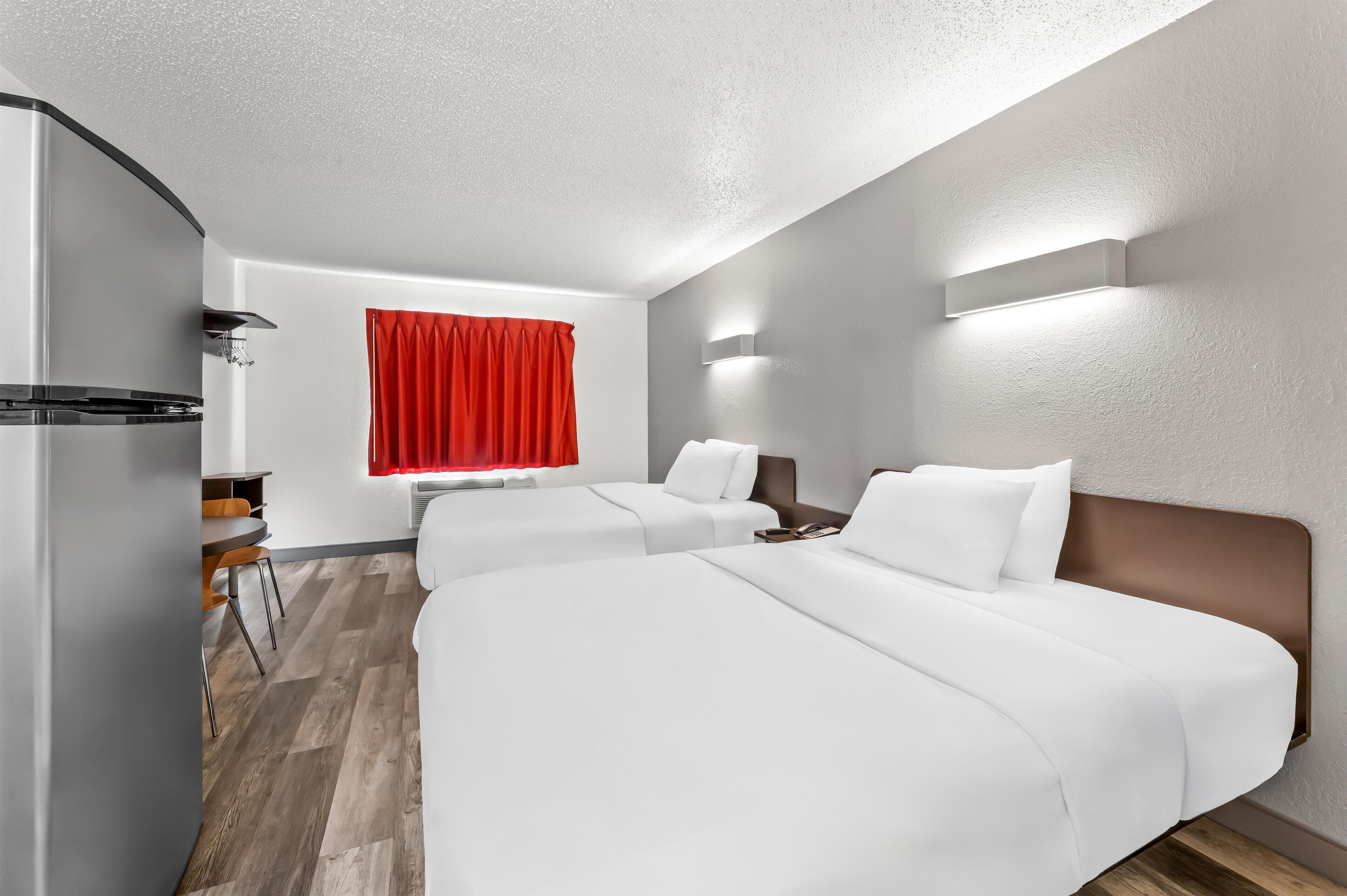 Habitación de hotel con dos camas, una zona de comedor y una cortina roja.