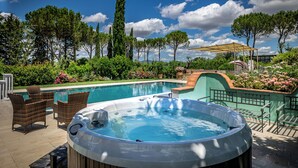Een hottub, zitplaatsen buiten en een zwembad, omgeven door groen en bomen.