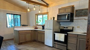 A modern kitchen with wooden cabinets, a built-in oven, a microwave, and a refrigerator. - Charming 2-bedroom cottage in Dexter with AC, WiFi. Enjoy your stay (Dexter)