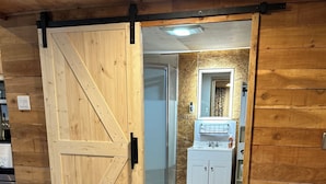 A room with a wooden door leading to a bathroom with a white sink and mirror. - Charming 2-bedroom cottage in Dexter with AC, WiFi. Enjoy your stay (Dexter)
