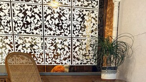 A wooden rocking chair with a woven backrest, positioned in front of a decorative wall panel with a floral pattern. - Charming 2-bedroom cottage in Dexter with AC, WiFi. Enjoy your stay (Dexter)