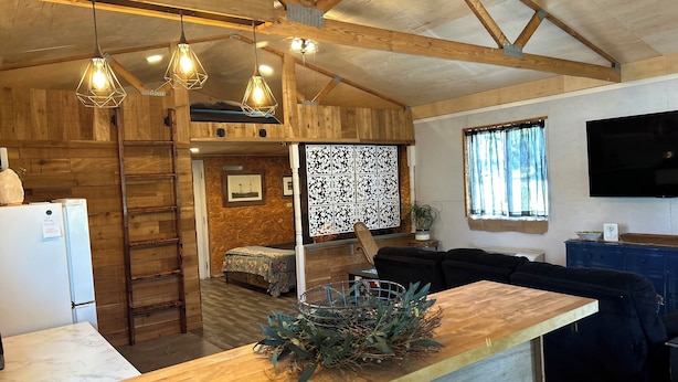 A rustic interior with exposed wooden beams, a wooden counter with a plant, a white refrigerator, a sofa, and a television. - Charming 2-bedroom cottage in Dexter with AC, WiFi. Enjoy your stay (Dexter)