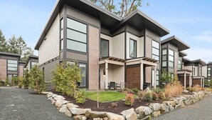 Una casa moderna de dos pisos con patio, borde de piedra y pequeños árboles.