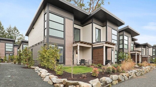 A modern two-story house with a patio, stone border, and small trees.