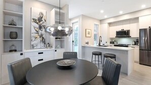 A modern kitchen with a central island, built-in appliances, and a dining area with a round table and chairs.