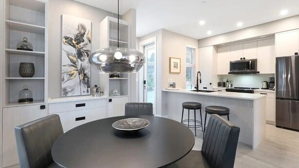 Una cocina moderna con una isla central, electrodomésticos integrados y un comedor con una mesa redonda y sillas.