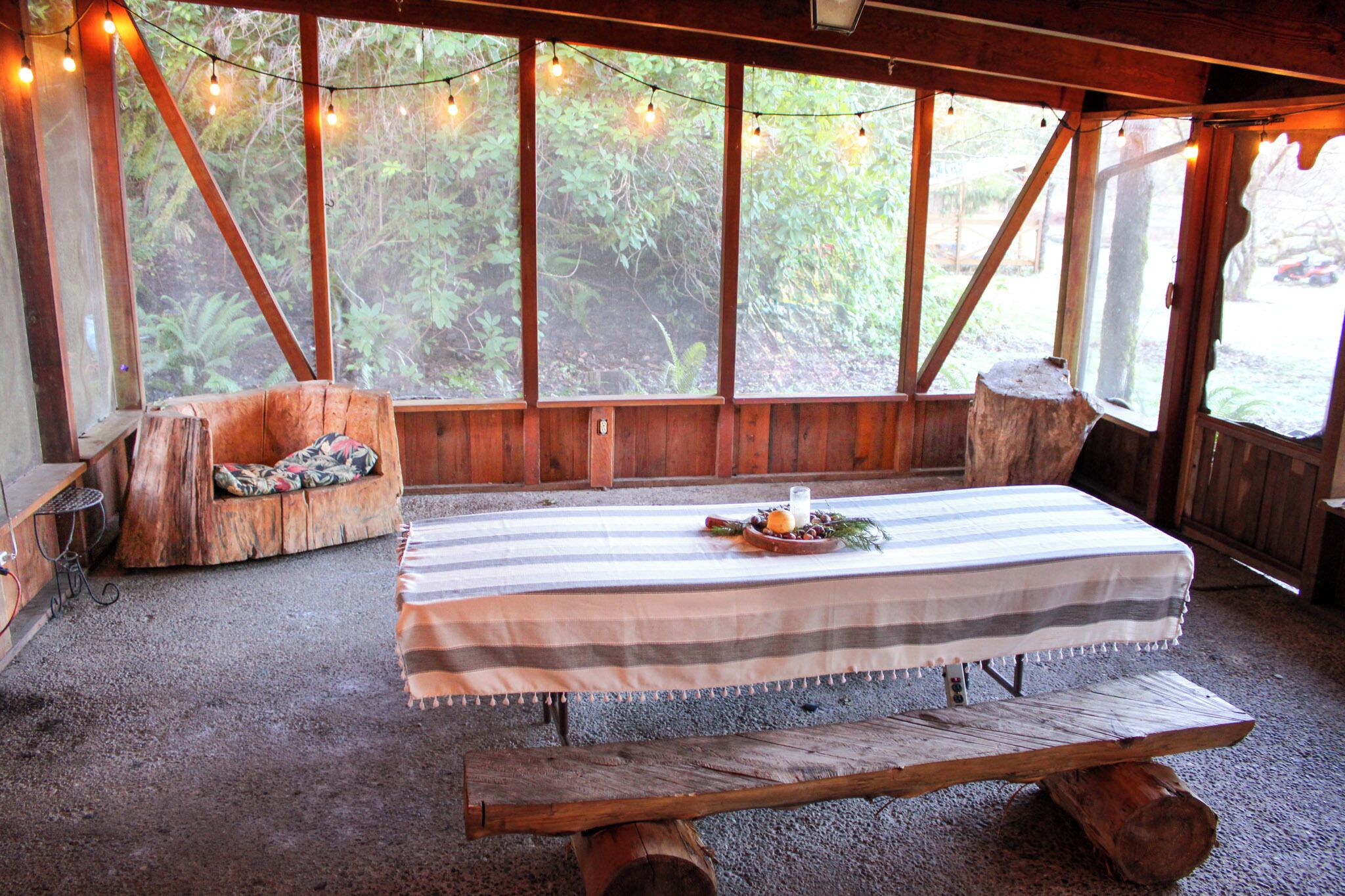 A rustic wooden room with a table set for dining, large windows with string lights, and a bench.