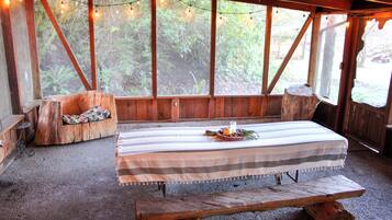 A rustic wooden room with a table set for dining, large windows with string lights, and a bench.