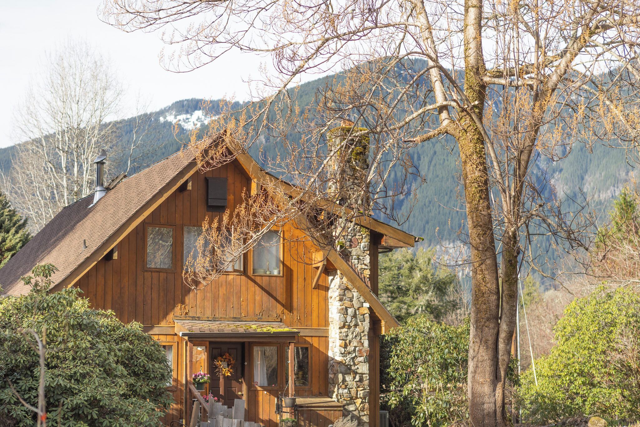 Une cabane en bois avec une cheminée en pierre, entourée d’arbres et de montagnes.
